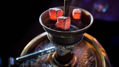 Glühende Kohle liegt auf einem Metallsieb über dem Tabak im Kopf einer Wasserpfeife in einer Shisha-Bar.  