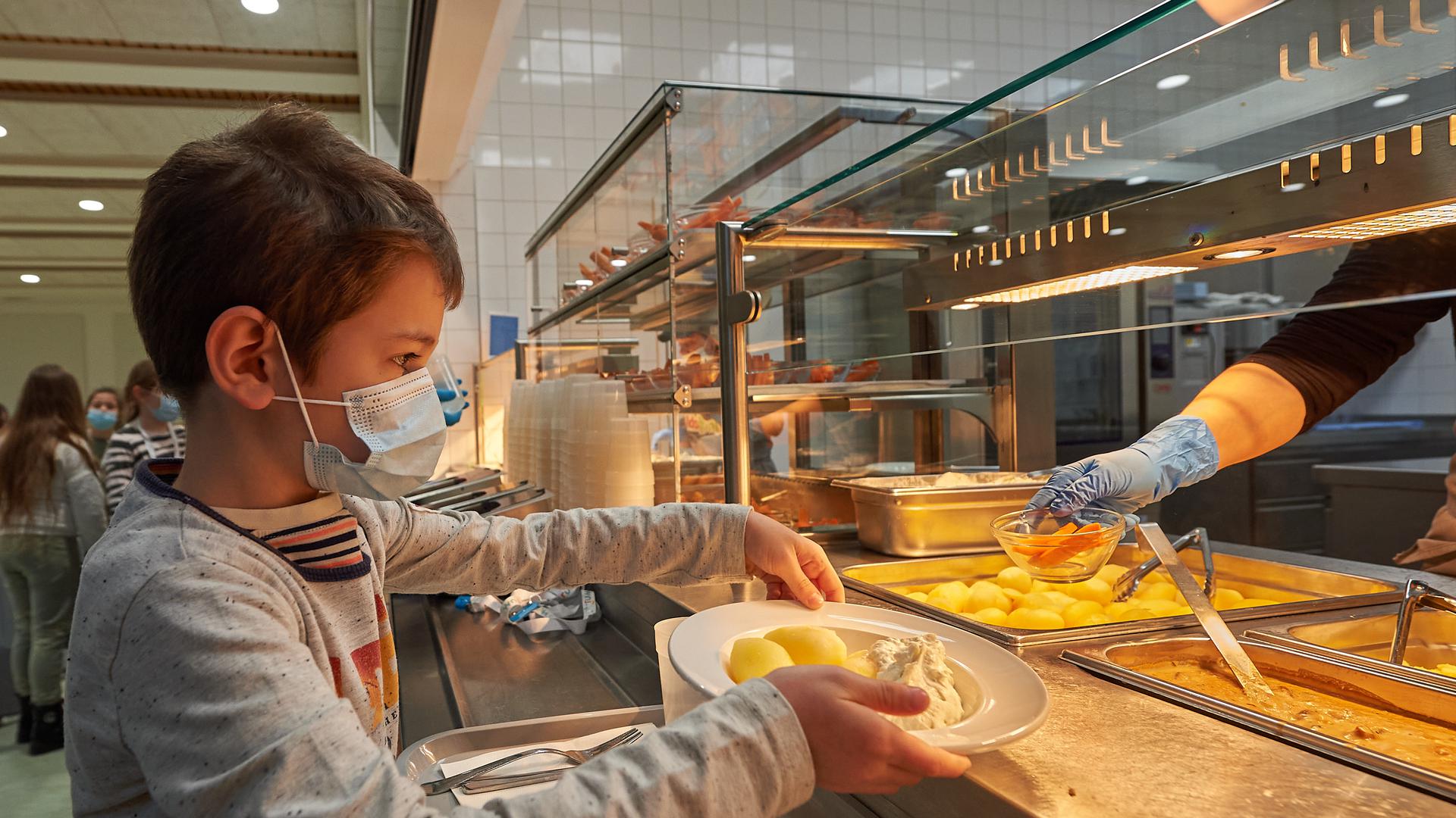 Schulmensa Stirumschule Bruchsal, ein Kind erhält einen Teller mit Essen an der Ausgabetheke.
