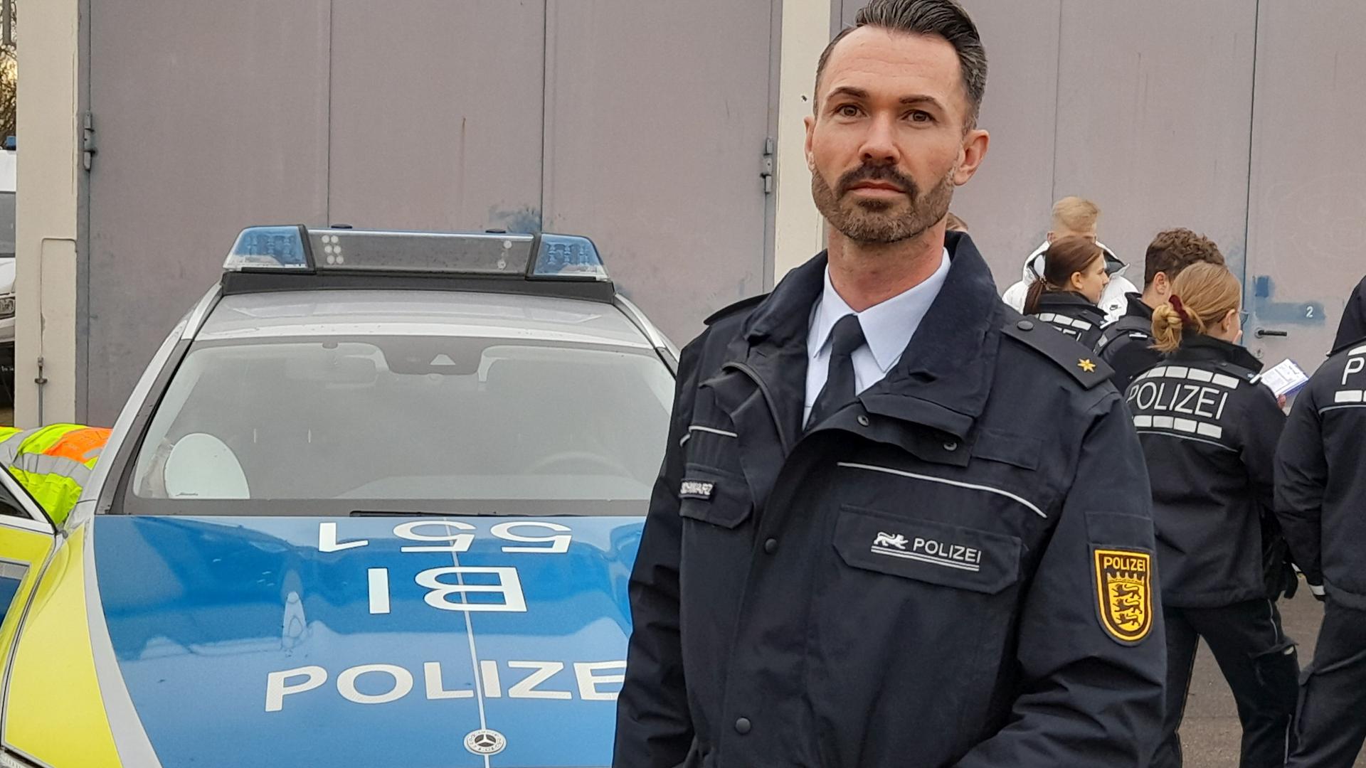 Sebastian Schwarz  mit Polizeischülern /-innen und vor einem Polizeiwagen.