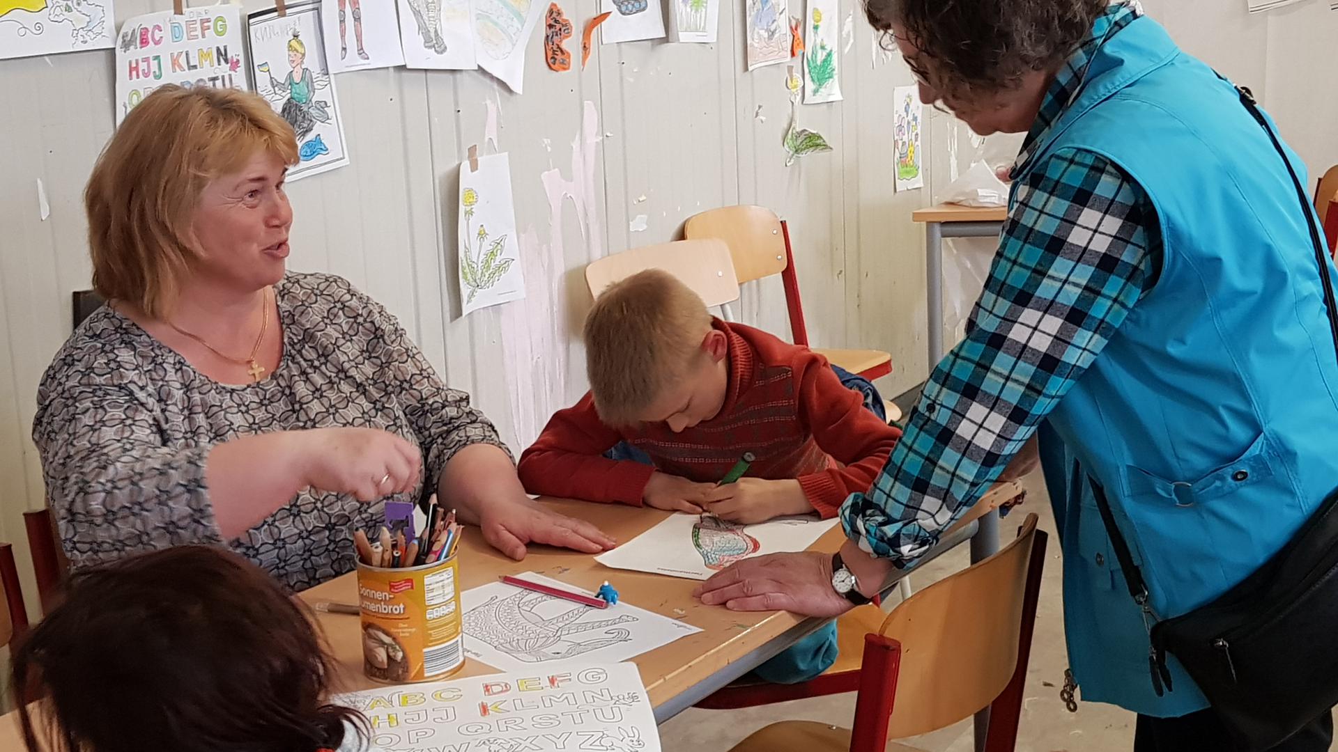 Die Ehrenamtliche Marliese Schwedes (rechts) und Vera unterhalten sich trotz Sprachbarriere „so gut es geht“, während der achtjährige Vanja eine Tiermandala ausmalt. 