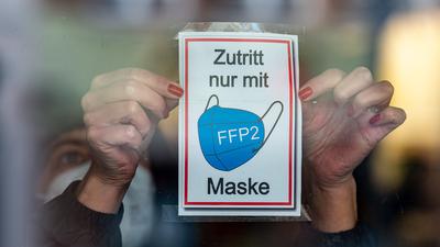 Eine Frau klebt ein Hinweisschild mit der Aufschrift „Zutritt nur mit FFP2 Maske“ an eine Glastür am Eingang eines Geschäfts in der Innenstadt. Niederbayern verschärft angesichts steigender Infektionszahlen seine Maßnahmen gegen die Corona-Pandemie. +++ dpa-Bildfunk +++