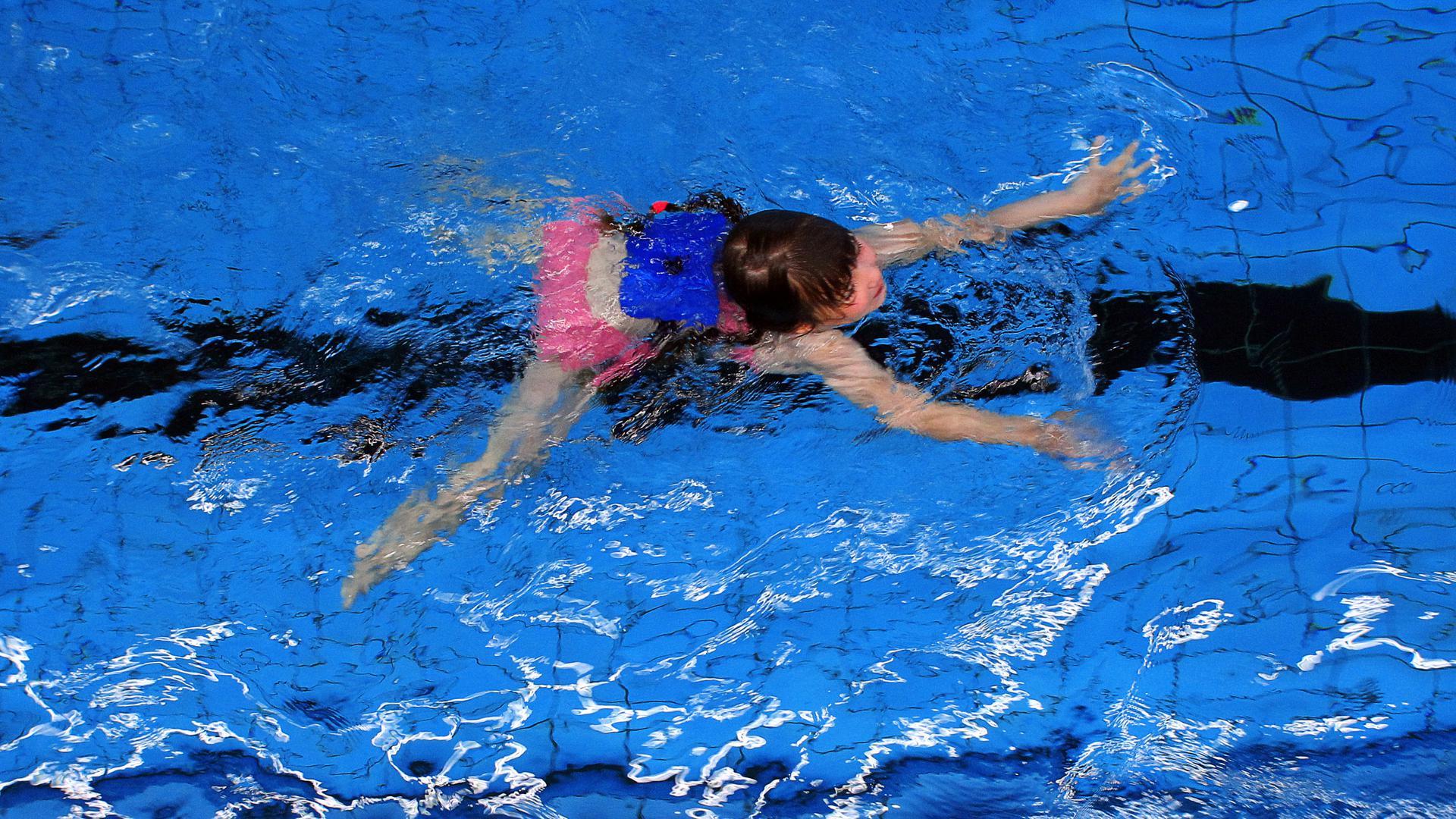 Ein Mädchen mit Schwimmhilfen im Becken einer Schwimmhalle, Symbolbild Schwimmkurs