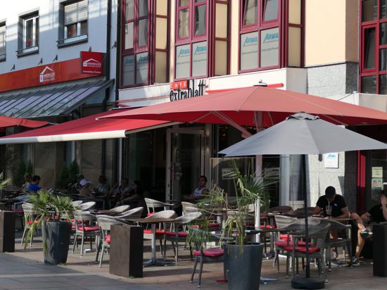 Außenbereich Cafe Extrablatt in Bruchsal. Gäste suchen gezielt den Schatten, Tische in der Sonne bleiben frei
