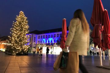 Eine Frau läuft mit mehreren Einkaufstaschen auf den Weihnachtsbaum auf dem Bruchsaler Marktplatz zu. 