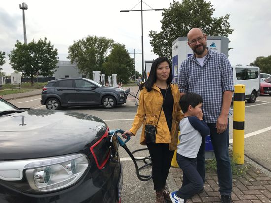 Eine Familie steht vor ihrem E-Fahrzeug auf der Raststätte Bruchsal-Ost. 
