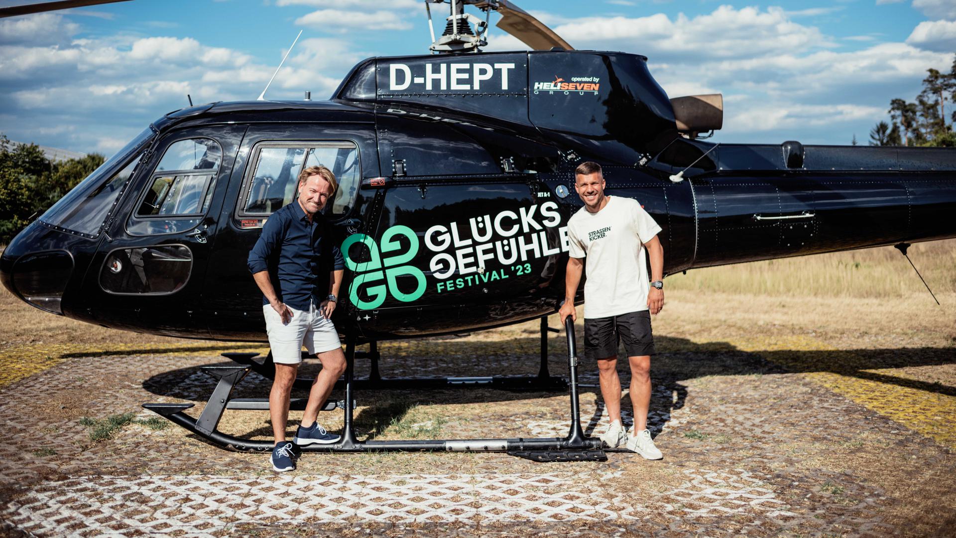 Lukas Podolski und Markus Krampe stehen vor einem Hubschrauber.
