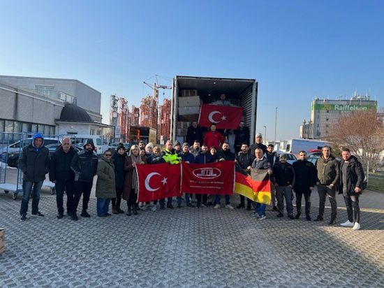 Laster mit deutsch-türkischen Fahnen und offener Tür, darin Pakete. Menschen drum herum