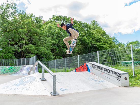 Ein junger Mann springt mit einem Skateboard über eine Rampe. 