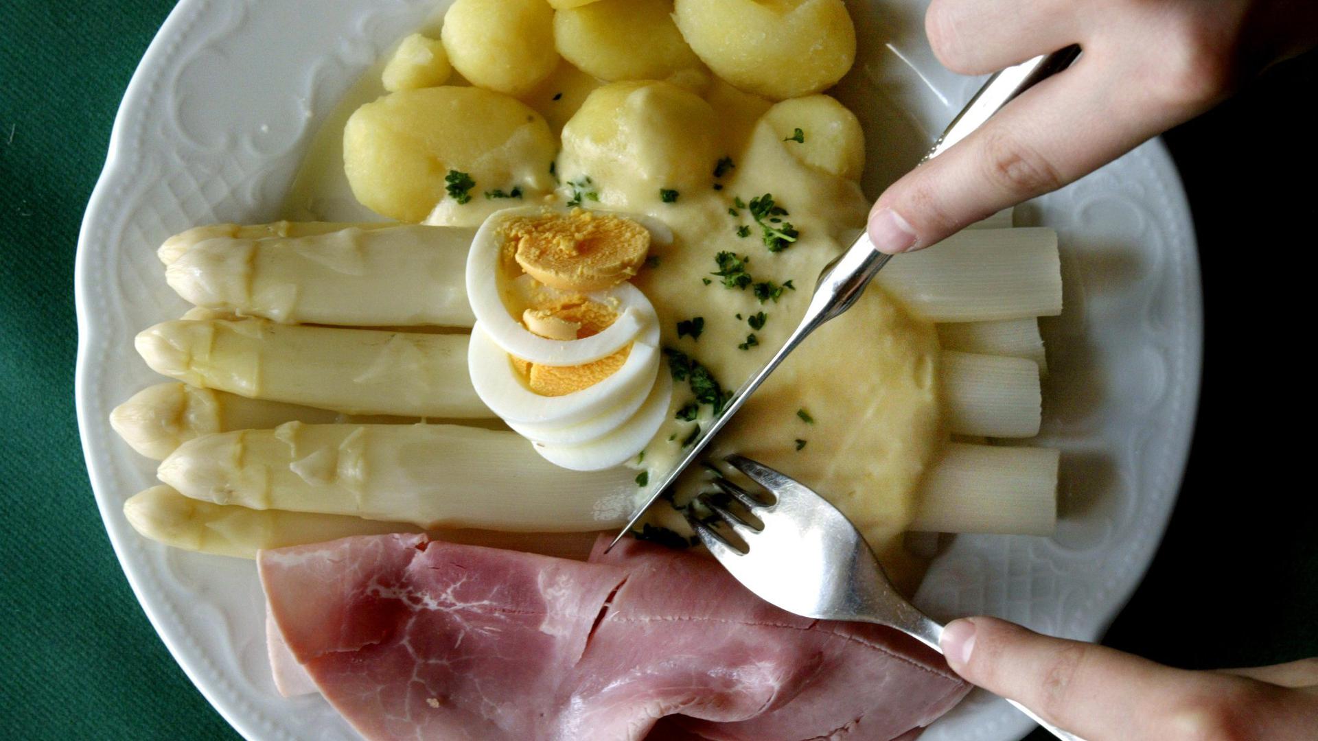 Eine Portion frischen Spargel mit Salzkartoffeln, gekochtem Schinken und "Sauce Hollandaise" isst  ein Gast in einem Spargelrestaurant. 