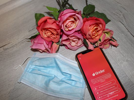 Strauß roter Rosen, Maske und Handy mit Tinder-Einstellung