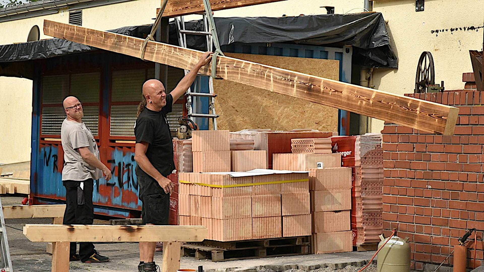 Zwei Helfer beteiligen sich am Umbau der Fabrik in Bruchsal. Ein langes Stück Holz wird gehalten.