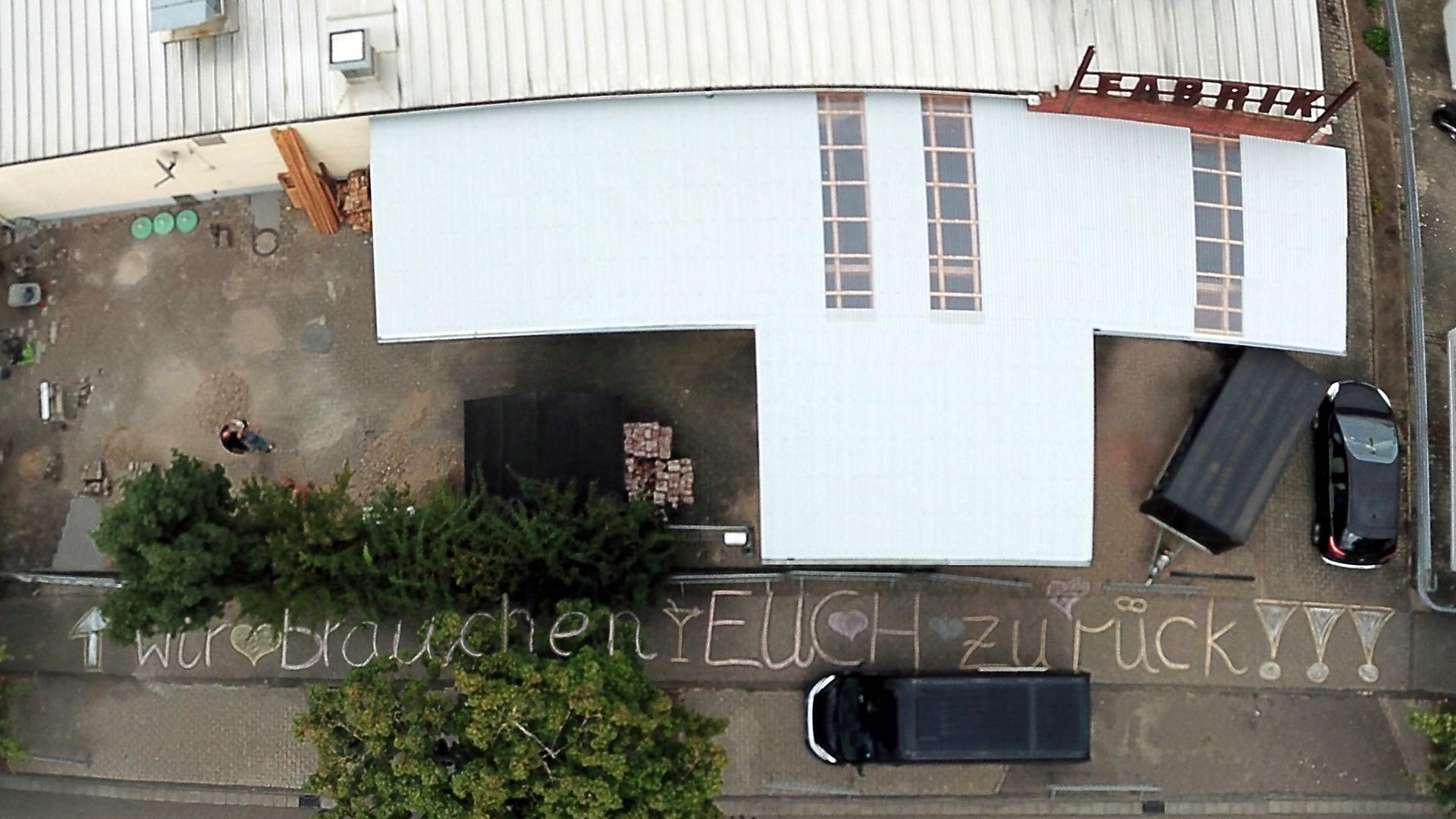 Luftbild auf Gebäude und Schrift „wir brauchen EUCH zurück“.