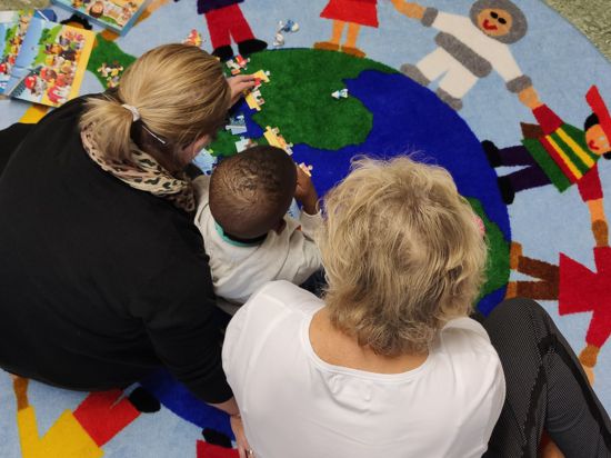 Ein Kind spielt mit zwei Betreuerinnen auf einem Teppich