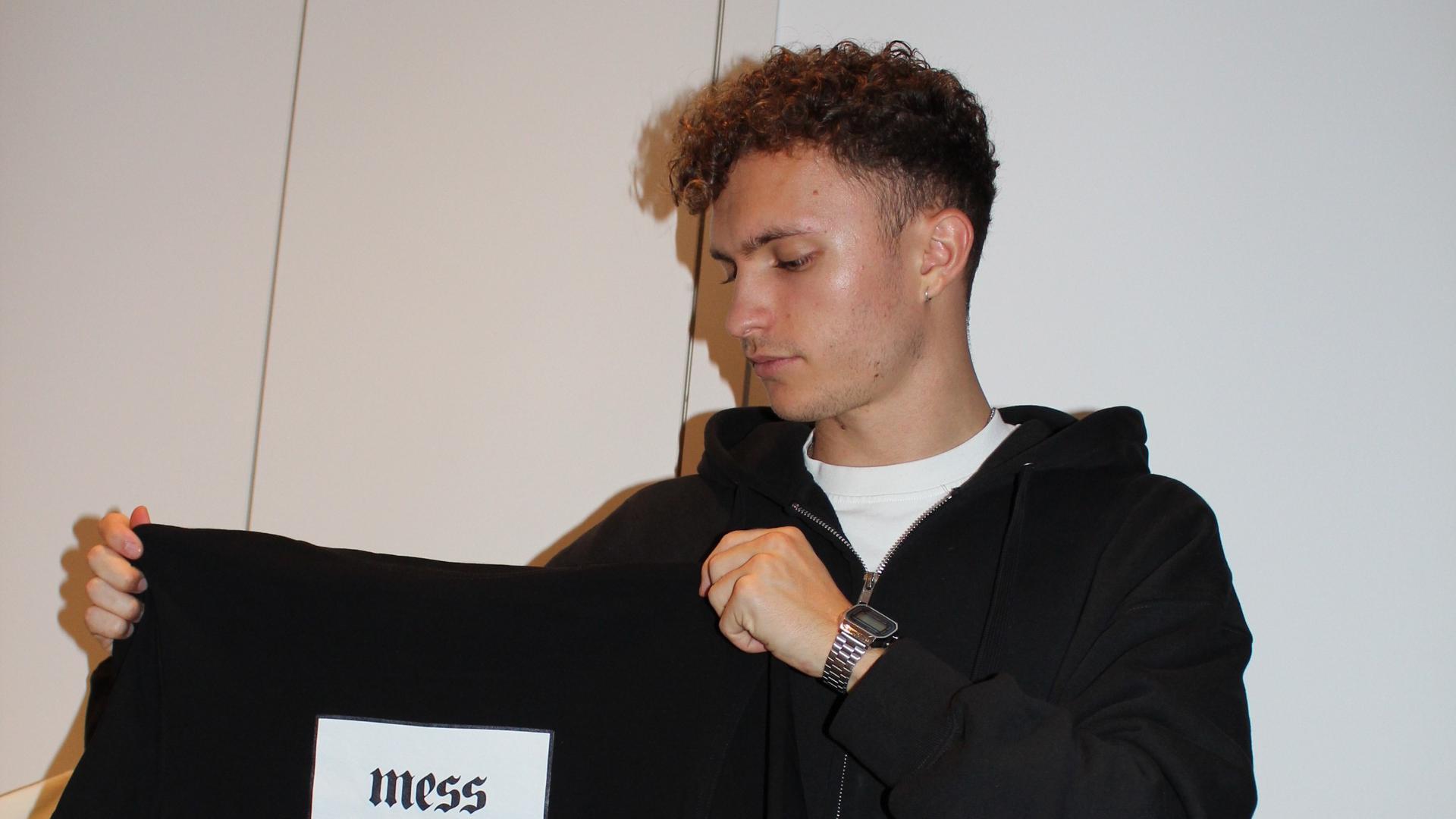 So sieht seine eigene Modemarke „kappotextiles“ aus: Noah Schmitt (22 Jahre alt, aus Karlsdorf) präsentiert eines seiner beliebtesten und meist verkauften T-Shirts, mit dem Aufdruck „mess“ auf der Rückseite