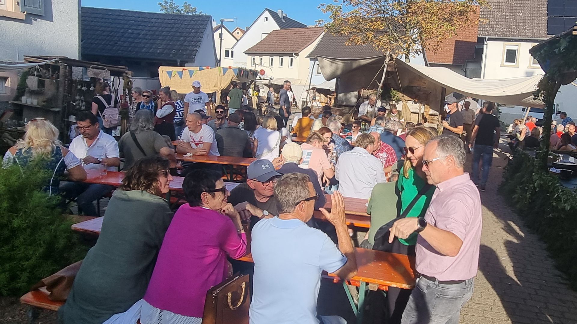 Menschen sitzen auf Bierbänken auf dem historischen Dorfmarkt in Oberacker.
