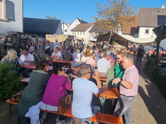 Menschen sitzen auf Bierbänken auf dem historischen Dorfmarkt in Oberacker.