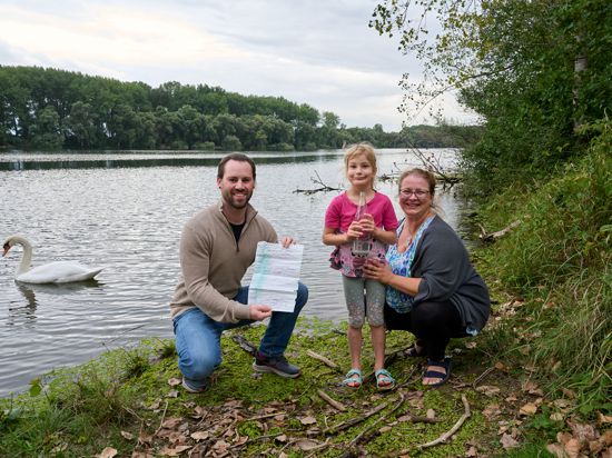 Marcel Metz, Janine Hofheinz und ihre Tochter Edda stehen mit Flaschenpost und Brief am Rheinufer in der Nähe der Insel Korsika in Oberhausen-Rheinhausen.