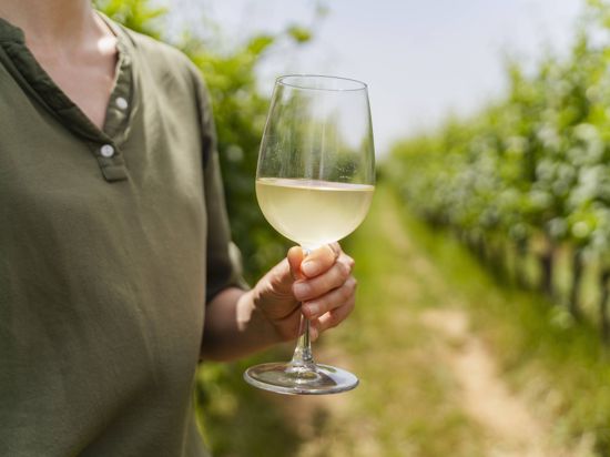 Eine Frau steht im Weinberg und hält ein Glas Wein in der Hand.