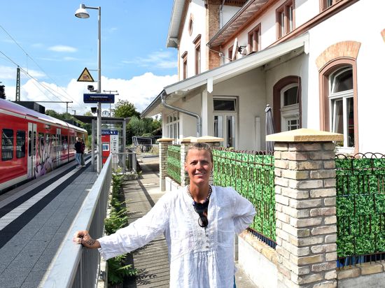 Randi Michels steht vor ihrem Bahnhofsgebäude in Rheinsheim. Im Hintergrund steigen Menschen in einen roten Zug ein.