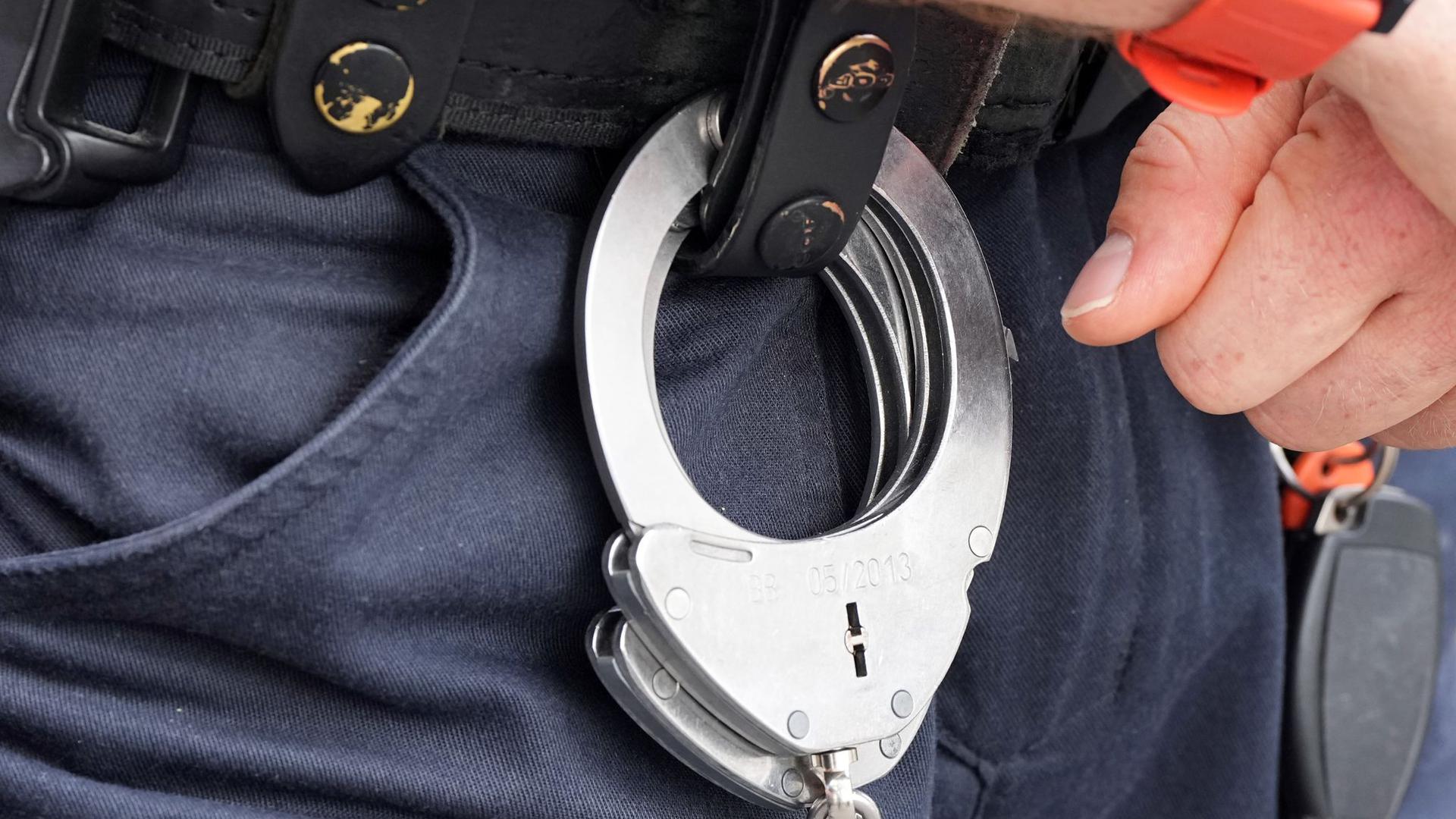 Handfesseln aus Metall hängen am Gürtel eines Polizisten.