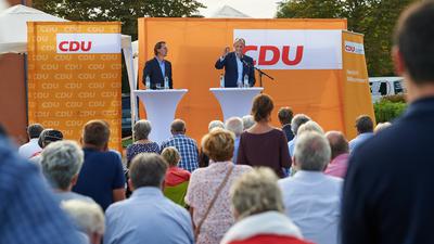 Zwei Männer auf einem Podium, dahinter Wahlwerbung der CDU. 