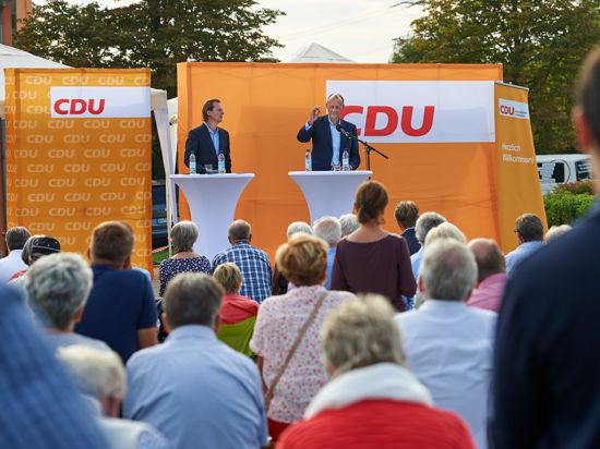 Zwei Männer auf einem Podium, dahinter Wahlwerbung der CDU. 