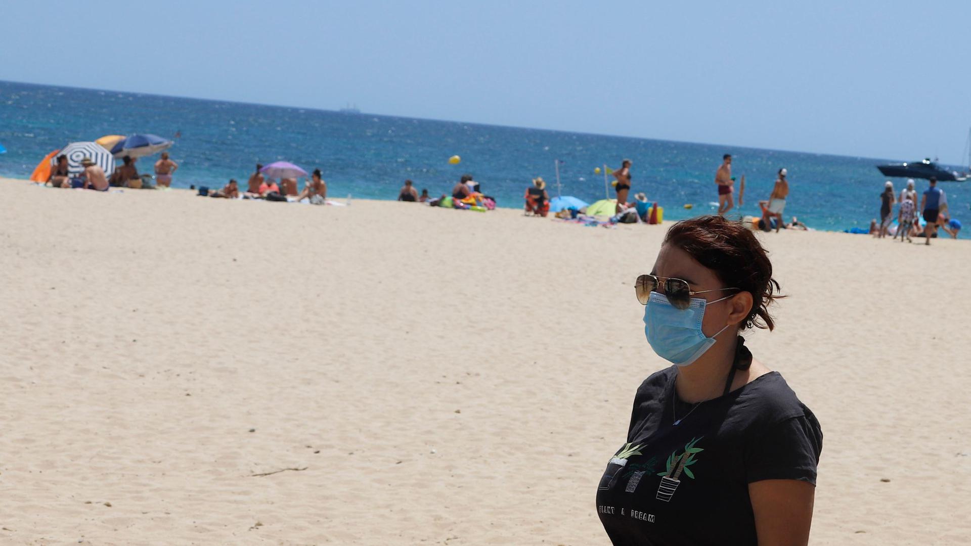 Eine junge Frau mit einer Schutzmaske an einem Strand.