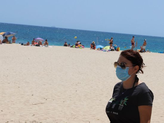 Eine junge Frau mit einer Schutzmaske an einem Strand.