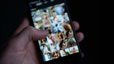 Ein Mann schaut sich auf einem Smartphone pornografische Bilder an. In Mittelbaden wurden wegen des Besitzes verbotener kinder- und jugendpornografischer Inhalte 14 Wohnungen durchsucht. 