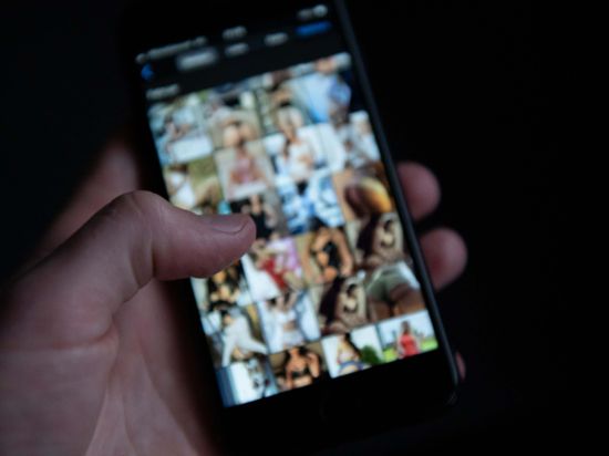 Ein Mann schaut sich auf einem Smartphone pornografische Bilder an. In Mittelbaden wurden wegen des Besitzes verbotener kinder- und jugendpornografischer Inhalte 14 Wohnungen durchsucht. 