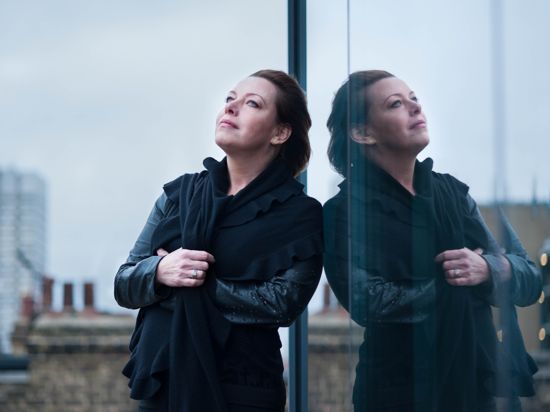 Nina Stemme lehnt an einer Glasfassade und blick versonnen in den Himmel