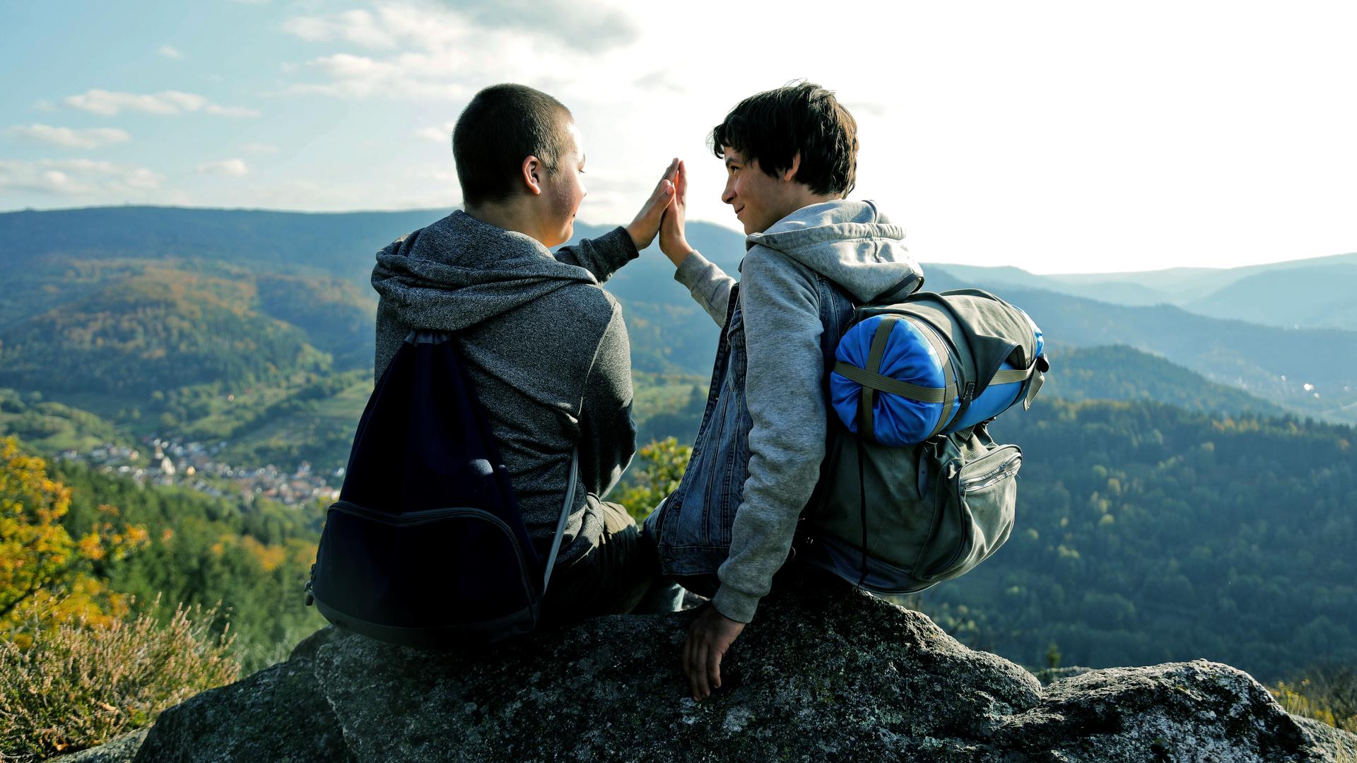 Zwei Jungen geben sich ein High Five vor einer Bergkulisse.