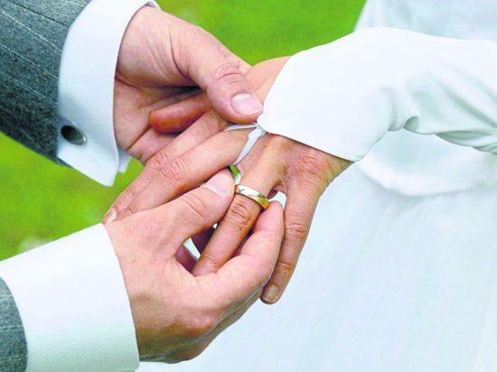 Ein Bräutigam streift bei der Trauung  seiner Braut den Ehering über den Finger. 
