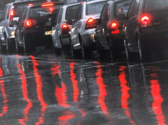 Die Bremslichter von Autos spiegeln sich bei Regen auf der Fahrbahn. 