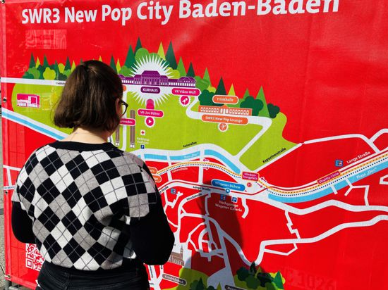 Eine junge Frau informiert sich an einem Transparent über die wichtigsten Standorte des Popfestivals im Jahr 2022.