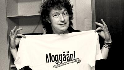 Wolfgang Niedecken hält in Baden-Baden ein T-Shirt mit der Aufschrift „Moggän“ in den Händen. 