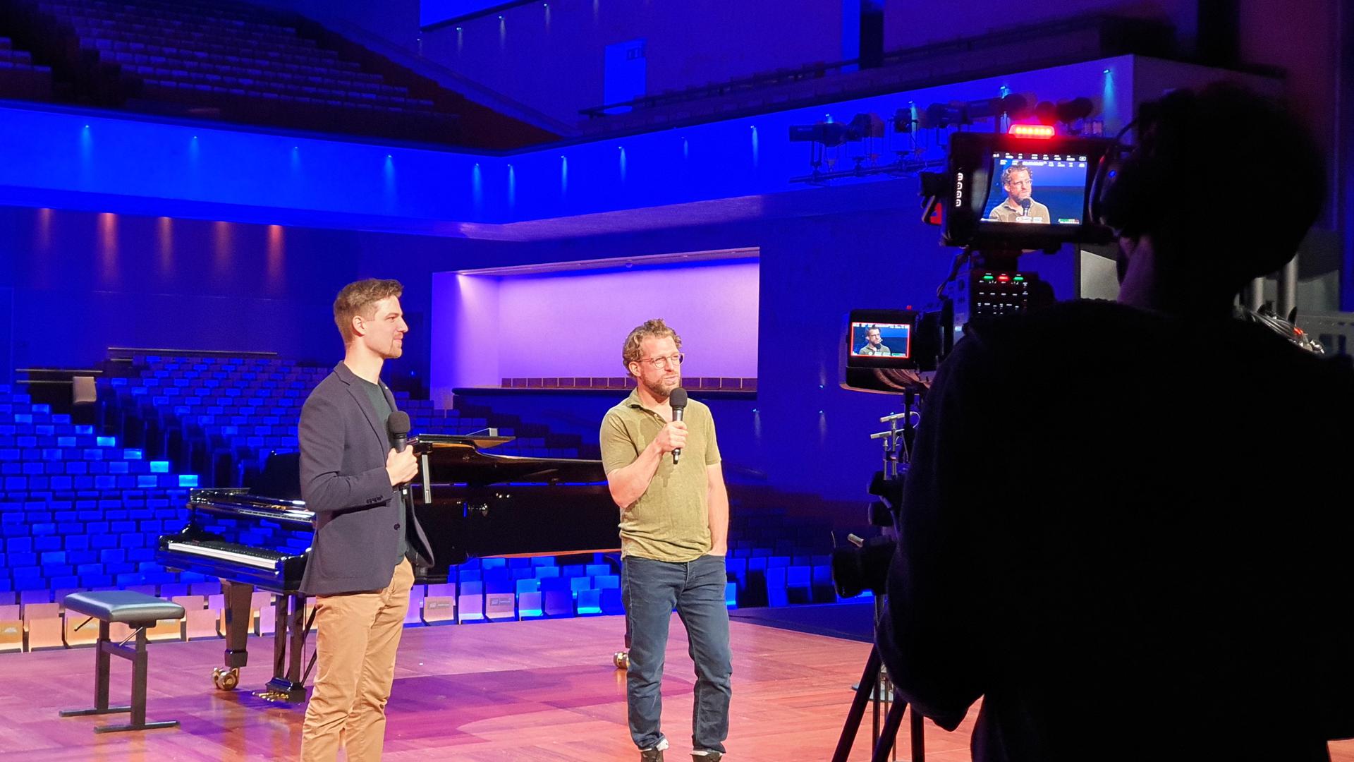 Der Projektverantwortliche Christian Vierling steht mit dem Sänger Julien Prégardien auf der Bühne des Festspielhauses. 