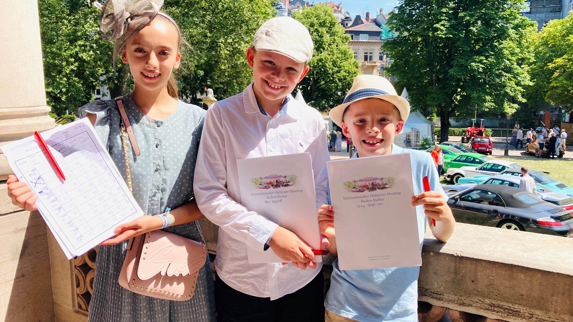 Nach einem selbst ausgearbeiteten Bewertungsbogen nimmt die Kinder-Jury mit Claire (von links), Maurice und Jean-Luc die Oldtimer beim Meeting in Baden-Baden unter die Lupe und vergibt drei Pokale. 