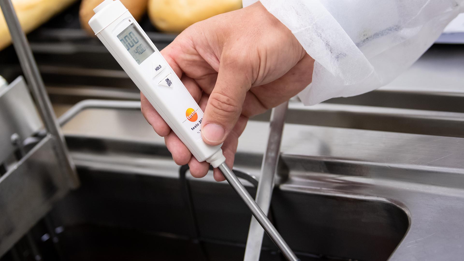 Hygiene im Blick: Ein Lebensmittelkontrolleur überprüft die Temperatur einer Friteuse in einem Restaurant.  