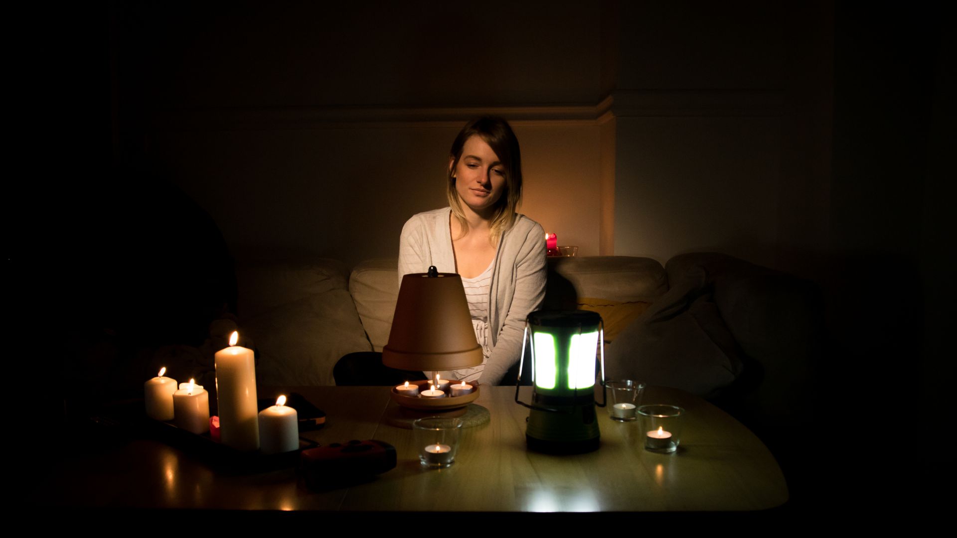 Eine Frau sitzt in einem lediglich mit Kerzen beleuchteten Raum.