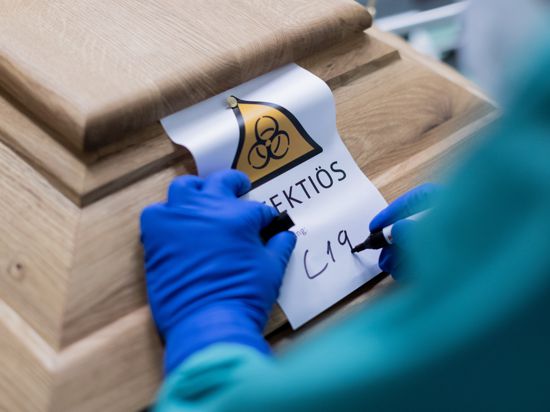 Christoph Kuckelkorn, Bestattungsunternehmer schreibt «C19» auf ein Schild mit dem Hinweis «Infektiös» auf einen Sarg mit einem Verstorbenen, der an oder mit dem Coronavirus gestorben ist. +++ dpa-Bildfunk +++