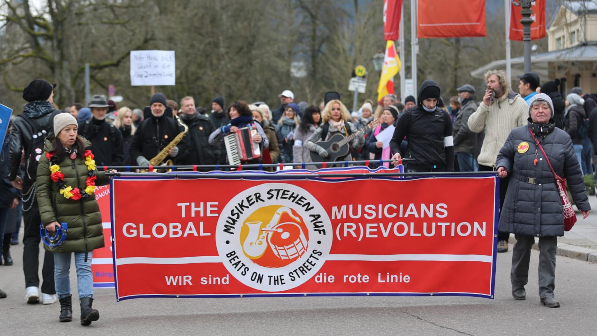 Zwei Frauen bei einer Demo halten ein Banner mit der Aufschrift „The Musicians Global (R)Evolution“