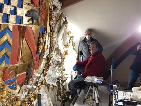Zwei Männer unterm Dach vor einem sehr großen Wappen