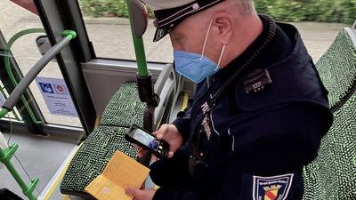 Ein Ortspolizist überprüft in einem Bus einen Fahrgast mit gelbem Impfbuch.