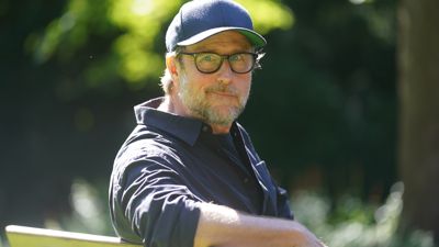 Der Schauspieler und Regisseur Bjarne Mädel sitzt auf einer Bank.