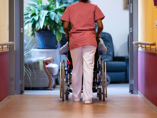 Eine Bewohnerin eines Pflegeheims wird von einer Pflegerin einen Gang entlang geschoben.