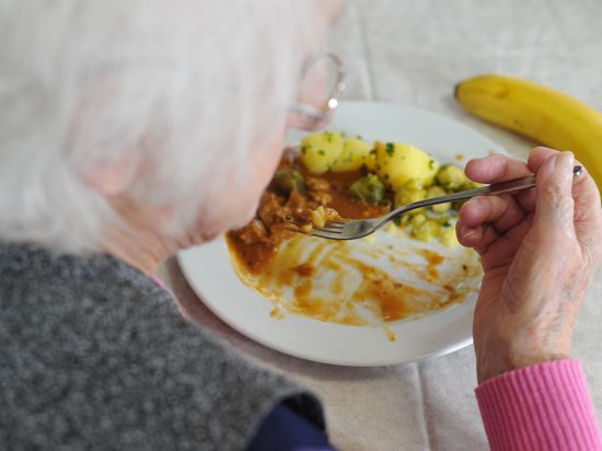  Eine ältere Frau sitzt in einem Seniorenheim und isst.