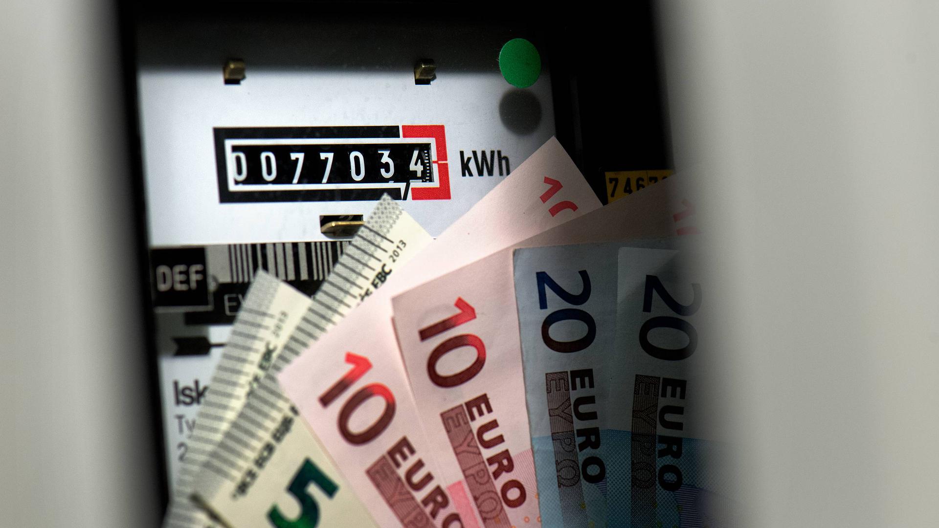 Geldscheine sind vor einem Stromzähler in einem Stromkasten in einem Haus zu sehen.
