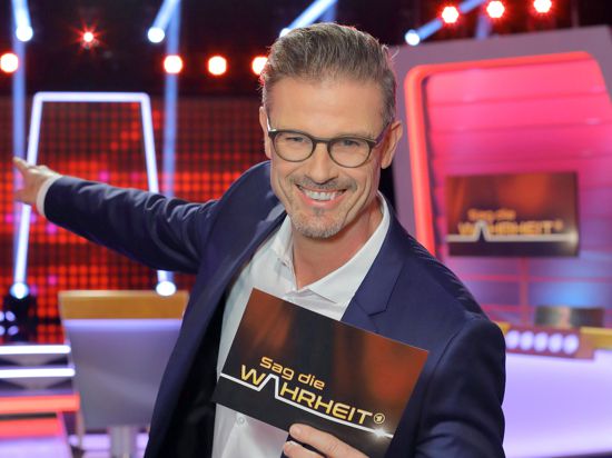 TV-Moderator Michael Antwerpes steht im Studio vor der Kulisse der Rate-Show „Sag die Wahrheit“.