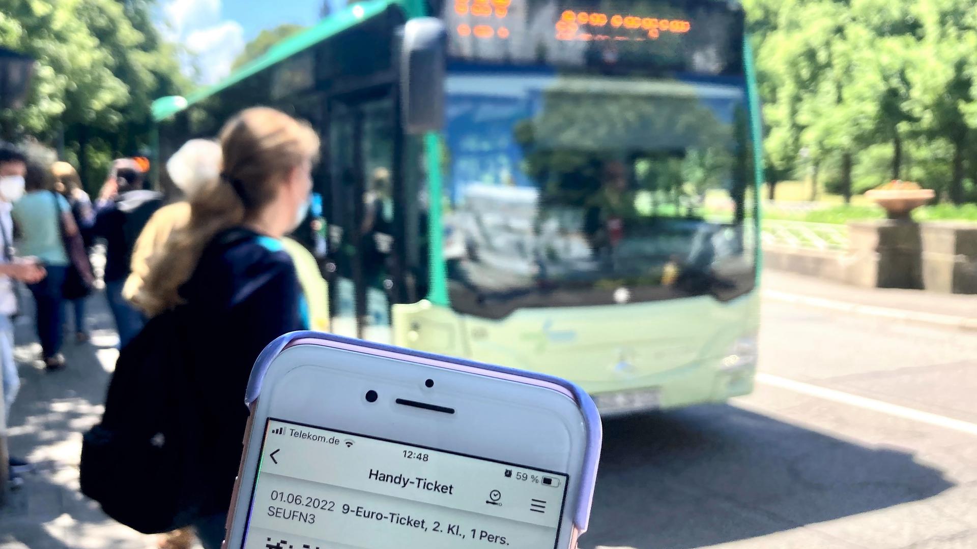 Ein Fahrgast zeigt an einer Bushaltestelle in Baden-Baden sein digitales 9-Euro-Ticket auf dem Handy.